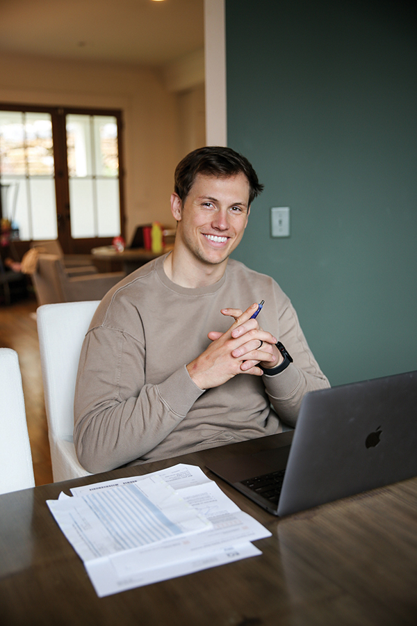 man siiting at table with papers and computer smiling at camera